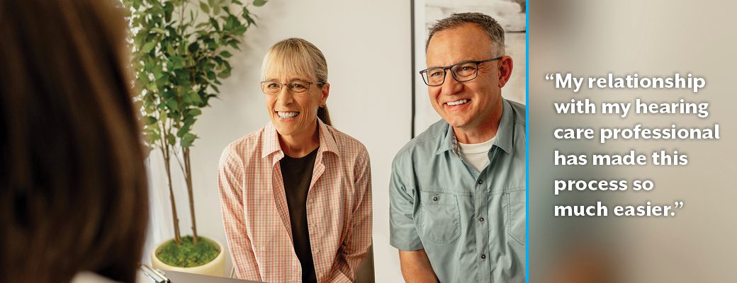 Image of Omega hearing aid wearer Daphne and her husband with her hearing care professional who has made the process so much easier for her